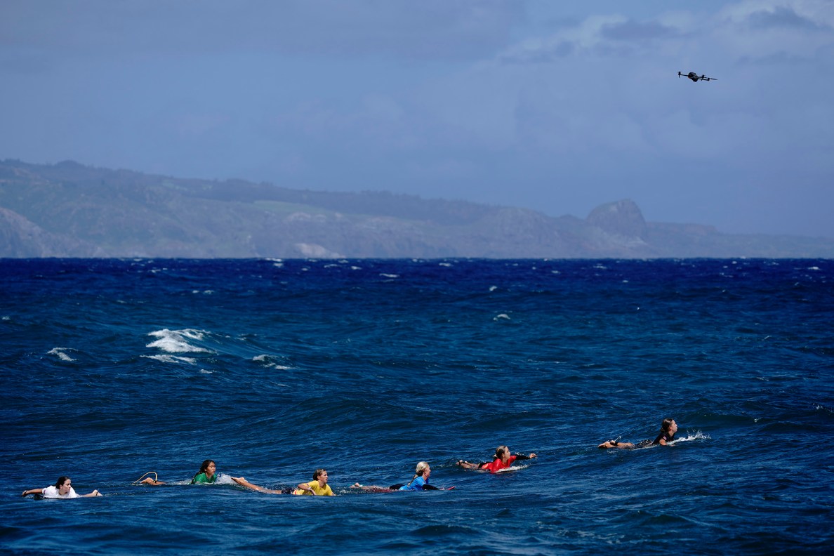 The inaugural Hawaiʻi High School Athletics Association surfing championships girls shortboard semifinal paddles toward the set of incoming waves as a drone flies overhead Saturday, May 2, 2026, at Hoʻokipa Beach Park in Pāʻia. (Kevin Fujii/Civil Beat/2026)