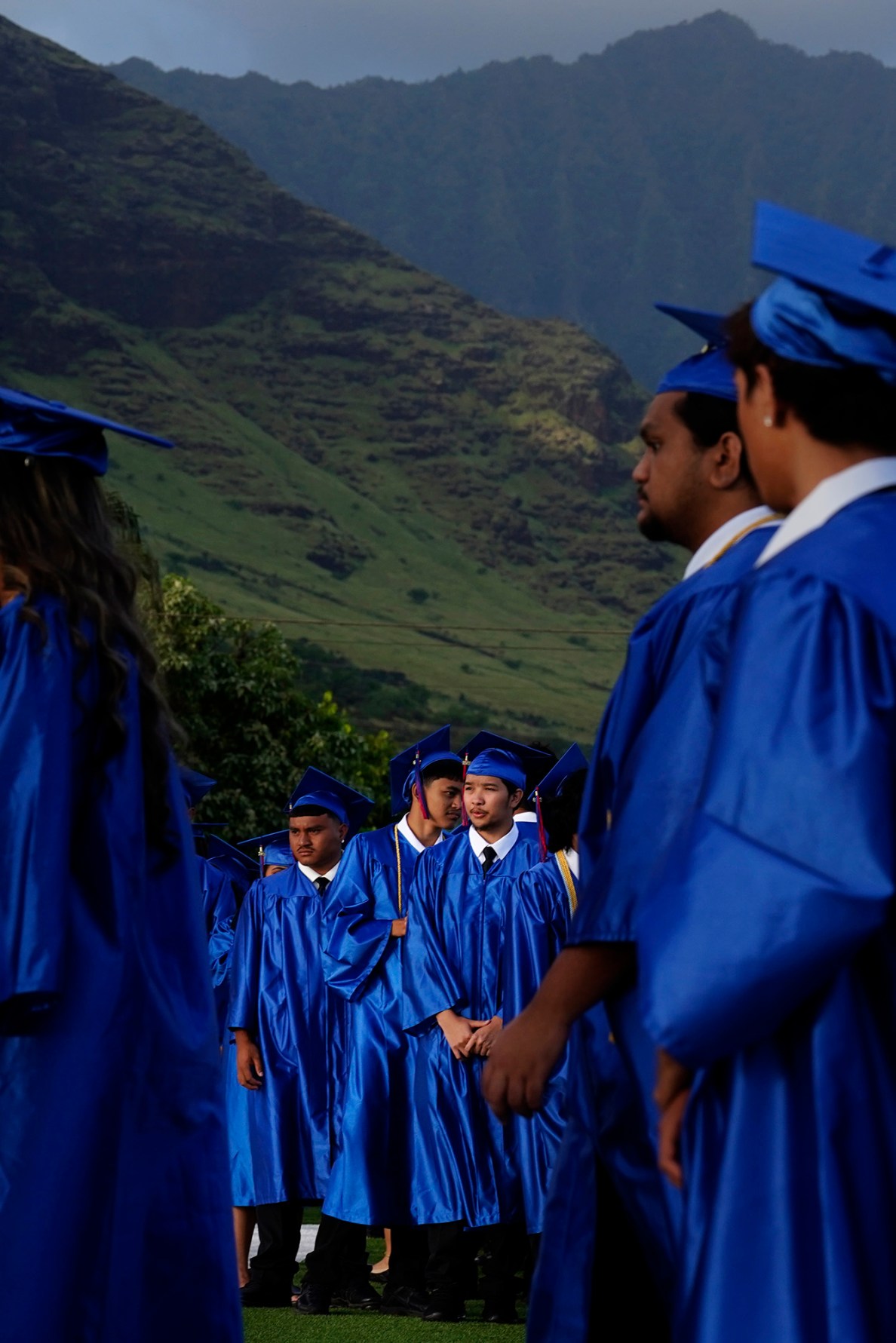 The Waiʻanae Mountain Range rises behind Waiʻanae High School seniors in cap and gown as they enter their commencement ceremony Friday, May 22, 2026, in Waiʻanae. (Kevin Fujii/Civil Beat/2026)