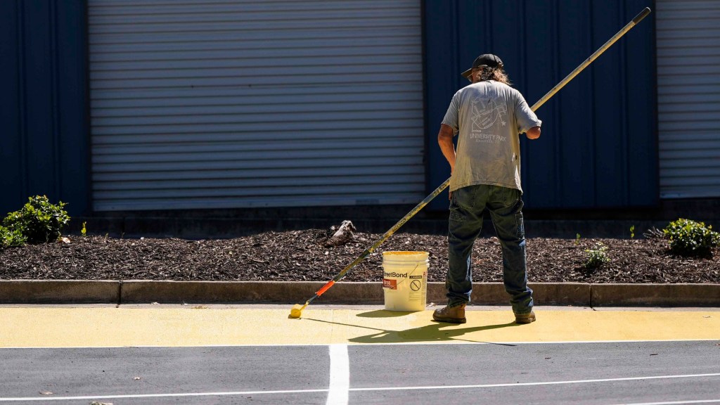 FILE - Ronnie Jefferies paints the parking lot at Science, Arts and Entrepreneurship School to help cool it by making it more reflective, Sept. 4, 2024, in Mableton, Ga. (AP Photo/Mike Stewart, File)