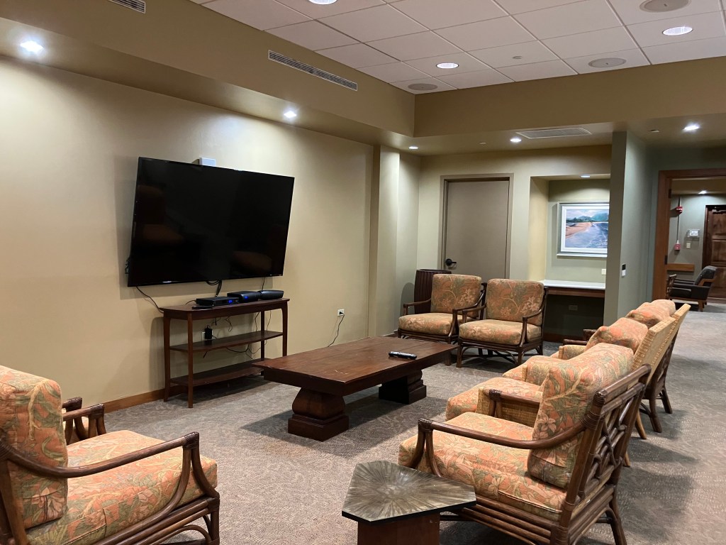 A large wall-mounted flatscreen tv facing eight cane lounge chairs.