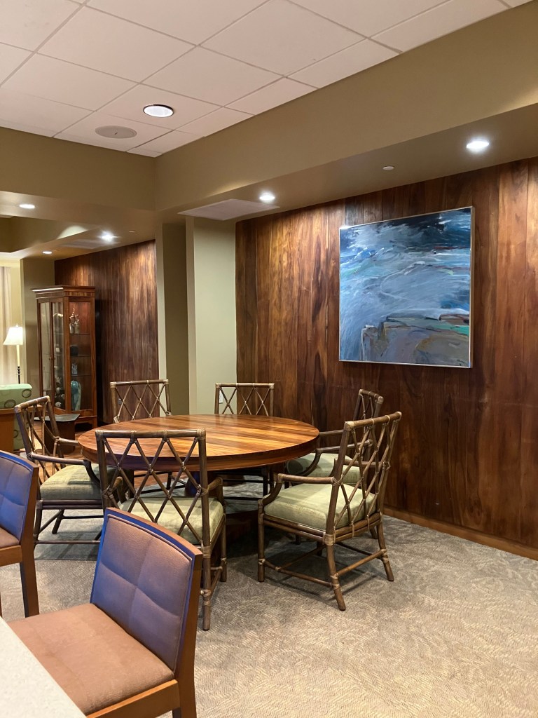A blue-colored painting hanging on heavy wood panels with large dining table and bar chairs.