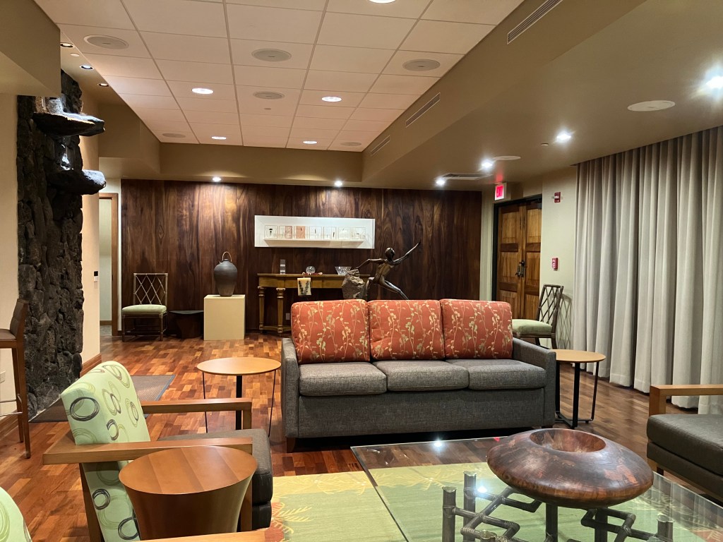 Long room with couches and chairs and various ornaments with downlighting, wood panels and heavy curtains.