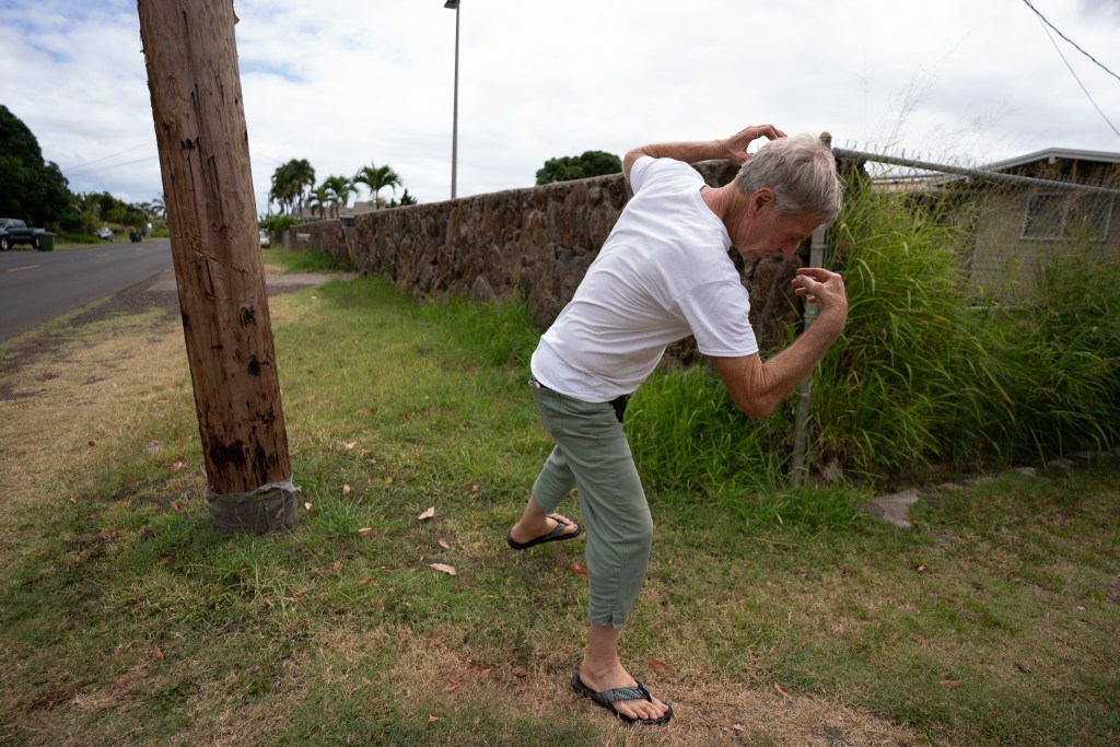 Xavier Staub recounts the March 27, 2026 attack by several dogs from the compound (background) next to his home on Mākaha Valley Road June 10, 2026. He suffered bite wounds to his left arm, leg and face, and fell to the ground striking his right elbow. He was able to get up while a dog had its jaw clamped to his face, he said. (Craig Fujii/Civil Beat/2026)