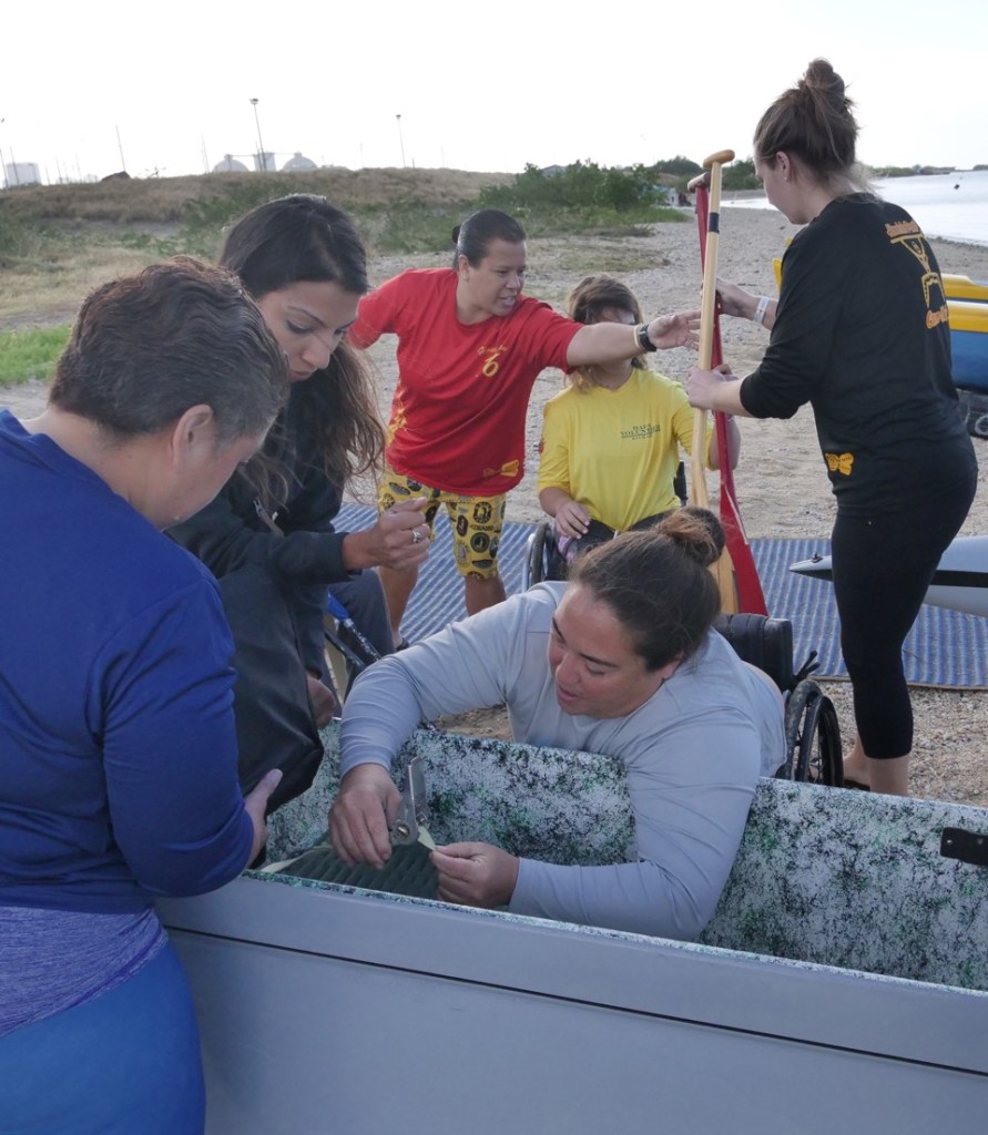 Volunteers from AccessSurf, AccessPaddling, HAPA, the Honolulu Pearl Canoe Club, the the Oahu 1st service platoon modify a canoe seat for Ann Yoshida (center) so she can join them for paddling at Sand Island in Honolulu, HI, Saturday, February 29, 2020. The AccessSurf adaptive paddling event brought together disabled community members and volunteers to make padding accessible for everyone. (Ronen Zilberman photo Civil Beat)