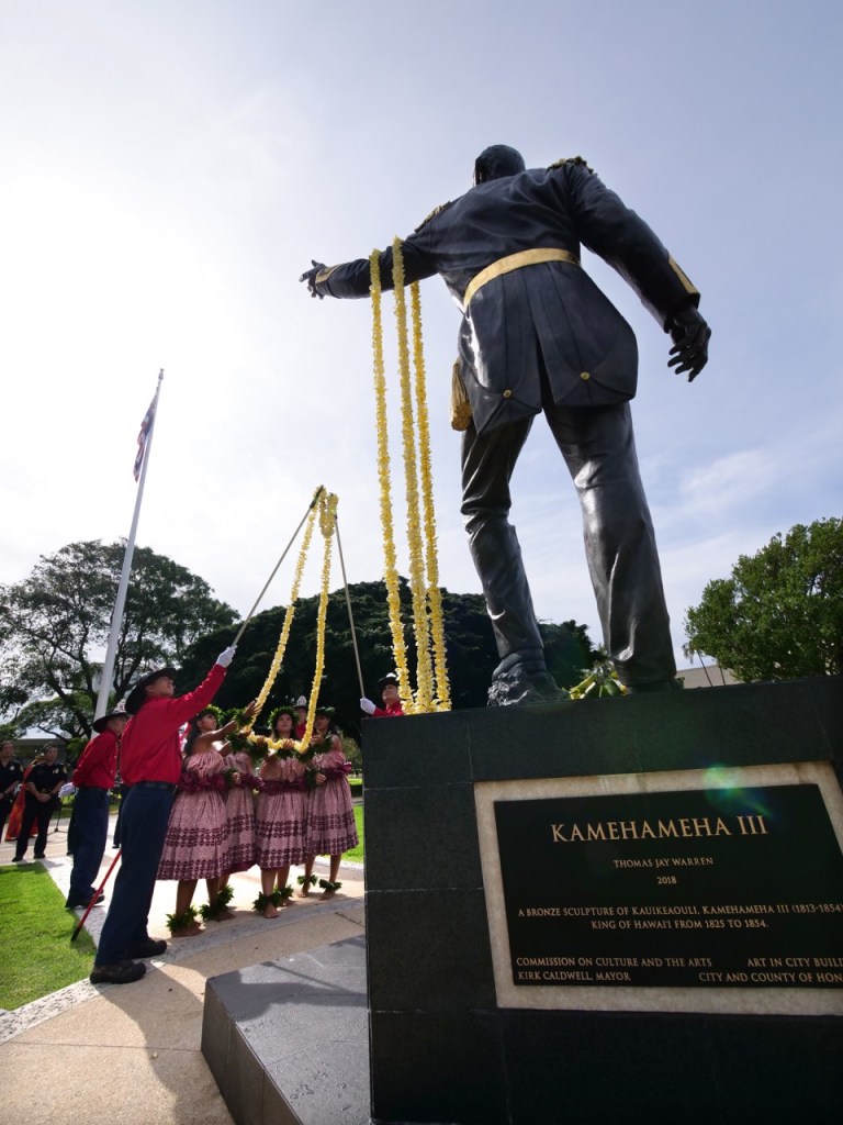 Halau Kau-La-Kahi dancers drape leis, with the help of Honolulu Fire Dept. personnel, onto a statue of King Kamehameha III at Thomas Square Park in Honolulu, HI, Friday, March 13, 2020.  The ceremony was held to honor the March 17th, 1814 birthday of Hawaiian monarch. (Ronen Zilberman photo Civil Beat)