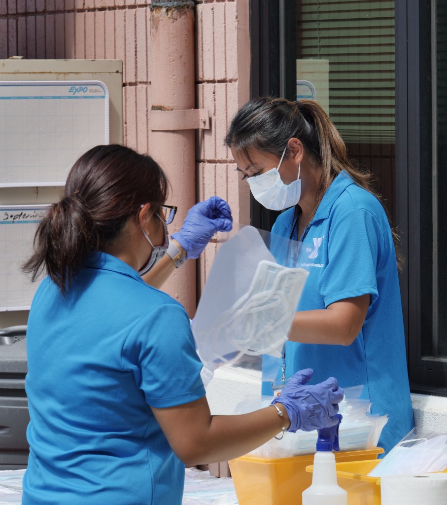Shyann Fermahin, left, and Renalyn Soriano sanitize bags of personal protective equipment (PPE) donations at the YMCA in Kalihi, HI, Thursday, April 9, 2020.  The YMCA in Kalihi is one of several non-profit organizations partering with the State of Hawai'i to become a "resilience hub" where community members can drop off homemade and unopened PPE gear to be distributed to behavioral health workers and social service providers statewide. The hubs will be open M-F from 9am - 11am for drop-offs. (Ronen Zilberman photo Civil Beat)