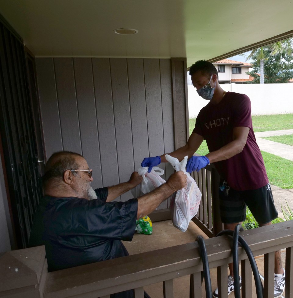 Pi'i Minns (right) delivers food to a homebound Kupuna in Kalihi-Palami on Monday, April 6, 2020.  The food pantry at Palama Settlement has remained open as an essential community service during the COVID-19 quarantines and they are accepting in-kind donations of fresh produce and unexpired canned goods to continue servicing high risk kupuna without transportation. (Ronen Zilberman photo Civil Beat)