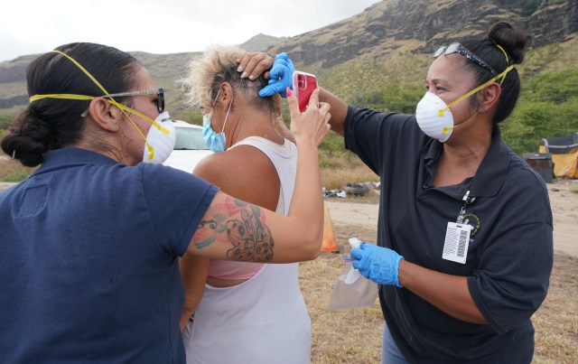 Dodie Rivera from the Waianae Coast Comprehensive Health Center assists with some outreach in Keeau, Waianae with left, Shaina McEntroe checking a homeless client camped on the beach. Both were checking on swelling from a centipede bite on the head during COVID-19 pandemic.