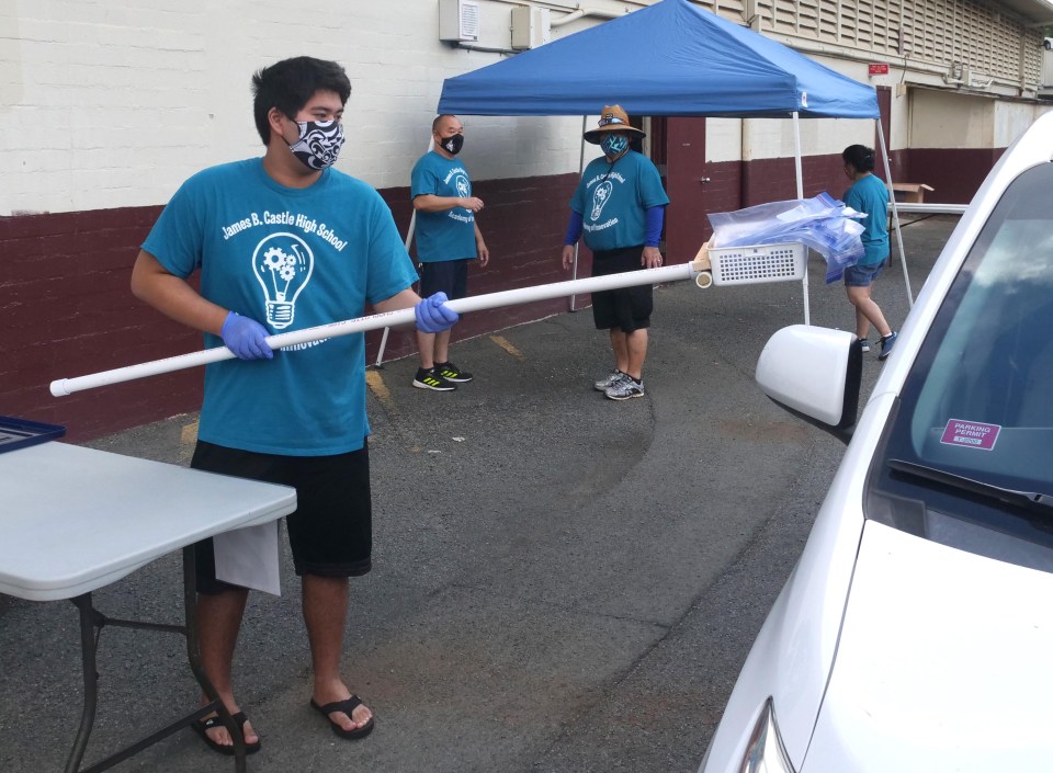 Volunteer Colby Cummins passes a STEM activity kit for kids into a Windward resident's car at Castle High School in Kaneohe, HI, Saturday, Oct. 3, 2020.  Castle High School students made about 1,500 Engineering Challenge activity kits to distribute to elementary and middle schools in the area for students and their families to enjoy and assemble over the fall break. (Ronen Zilberman photo Civil Beat)