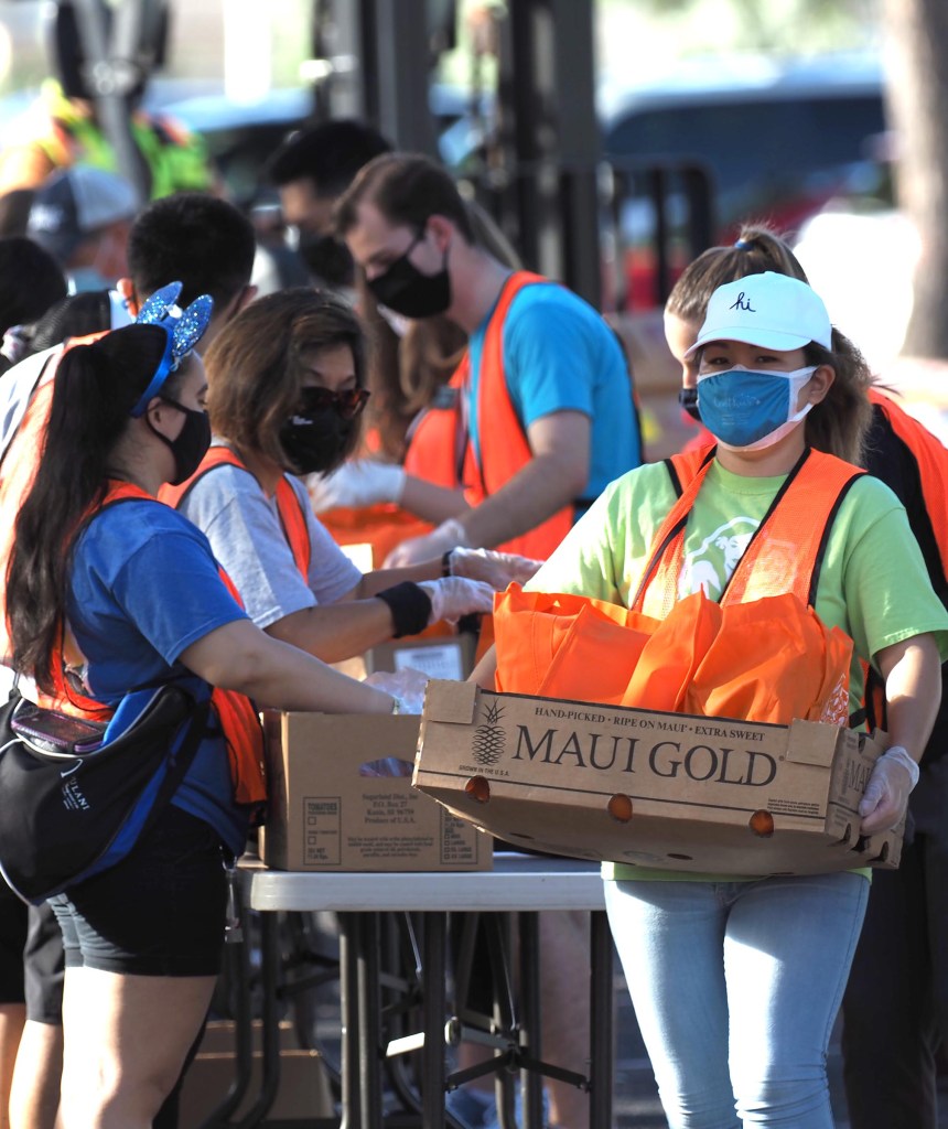 Volunteer carries box of fresh produce whilst others pack food into boxes to be distributed to the 2500 Hawai'i residents arriving at the Aloha Stadium Monday, November 16, 2020.  The food pop-up distribution was organized by the Hawaii Foodbank (Photo Ronen Zilberman/Civil Beat).
