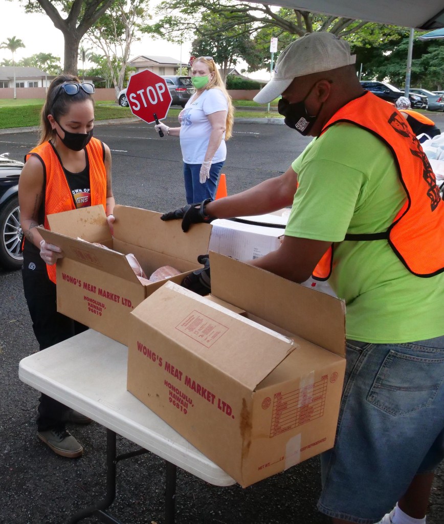 Rosalie Kamaka (left) a volunteer from the Pearl City Elks Lodge #2669 works together with Hawai'i Foodbank volunteer Rick Hanna as they unpack boxes of meat to be given out during a food distribution event, in Mililani, on Wednesday, December 16, 2020. (Ronen Zilberman photo Civil Beat)
