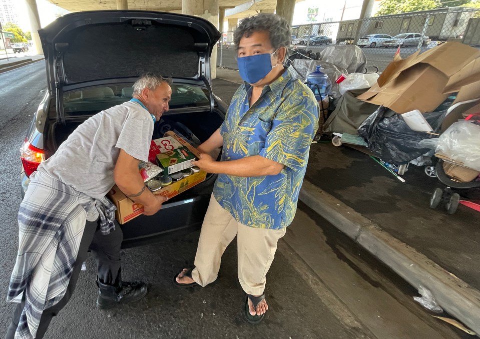 Bill Sheen distributes food he bought with his own money to a group of homeless individuals beneath the H1 freeway overpass at Kapahulu Blvd in Honolulu, on Wednesday, July 14, 2021. Sheen says he performs these acts of kindness on a daily basis. (Ronen Zilberman photo Civil Beat)