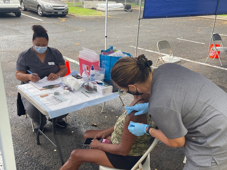 Project Vision Hawai'i nurses, Natasha Jackson (left) and Toni Floerke (right) process paperwork and administer a COVID shot to Johnnie Silva, a resident of the Honolulu Community Action Program's (HCAP) Kumuhonua transitional housing center in Barber's Point, HI, on Wednesday, July 14, 2021.  HCAP partnered with the Hawai'i Department of Health, The Hawaiian &amp; Pacific Islander Hawai'i COVID-19 Response, Recovery and Resilience Team and Project Vision Hawai'i to host the vaccination event at the center. (Ronen Zilberman photo Civil Beat)