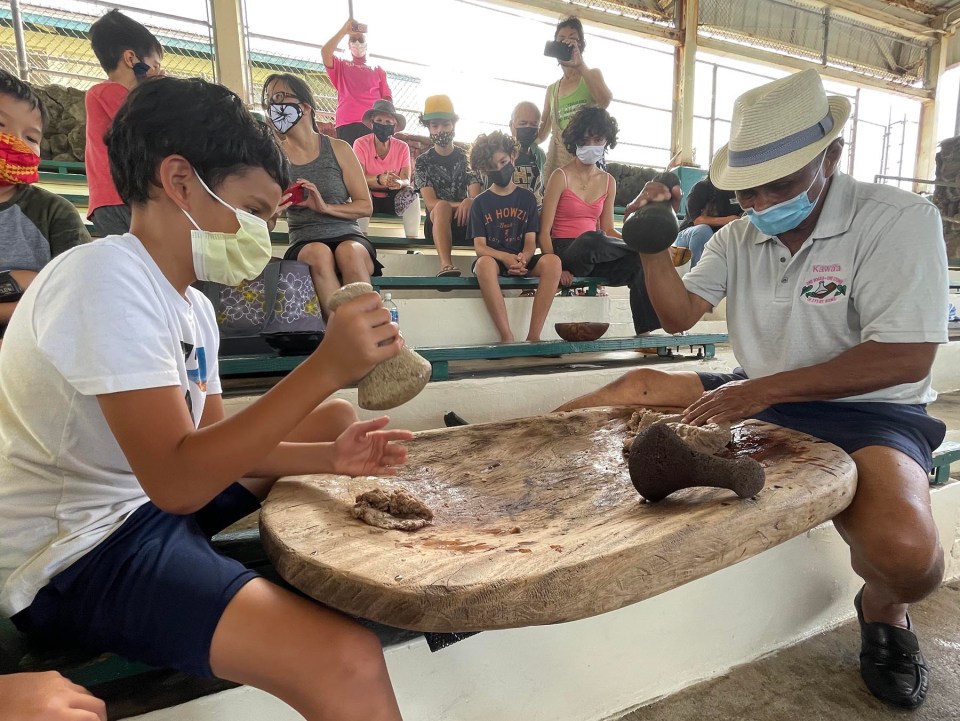 Kumu Earl Kawaa (right) passes down the Hawaiian tradtion of poi pounding (ku'i kalo) to Kaimalu Pomroy (left) and other participants during the Lā Ku'i Kalo I Papakōlea in Honolulu, Hawaii. Saturday July 24, 2021.  Like many other participants the Pomroy family appreciates the opportunity Papakōlea is providing for them to use their board and stones to make poi as a means to reconnect with their family, culture, community and the aina. (Ronen Zilberman photo Civil Beat)