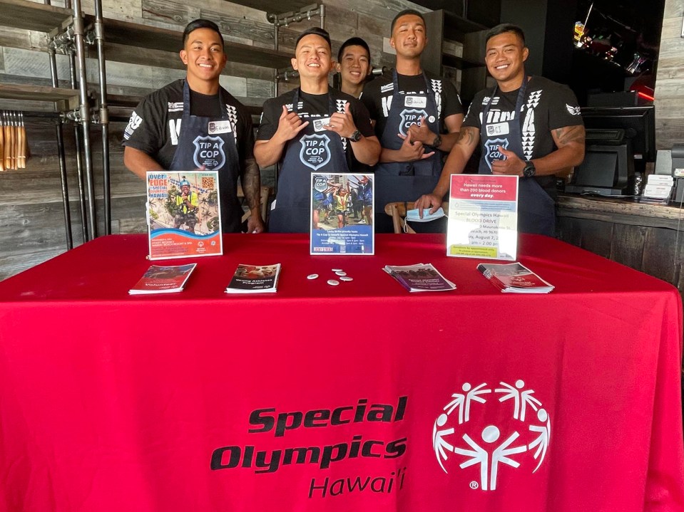 Honolulu police officers, from left, Edison Tagama, Garrison Gamio, Keenan Kihara, Uriah Simmons, and Christopher Oallasma volunteer to greet customers and assist servers at Lucky Strike, in the Ala Moana Shopping Center, to raise awareness for Special Olympic Hawai'i athletes, Sunday, July 18, 2021.  All proceeds raised from the "Tip a Cop" event will stay in the islands to help fund sports training, competitions, and programs for local athletes. (Ronen Zilberman photo Civil Beat)