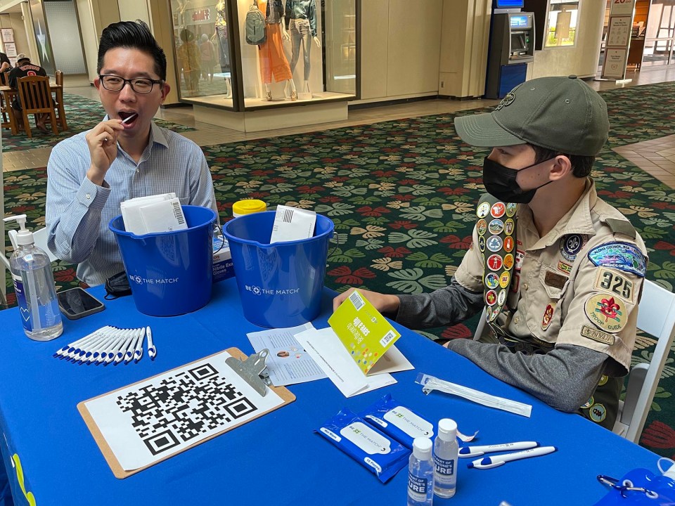 Hawaii State Senator, Stanley Chang (left) swabs his mouth as part of the process to become a bone marrow donor during a donor match drive organized by Eagle Scout troop 325 member Riley Regan (right), at the Kahala Mall, Friday, August 20, 2021. Regan was inspired by his dad's experience becoming a bone marrow donor to organize the drive, for his Eagle Scout project. His goal is to register 1,000 new people  with Be The Match Hawaii. Regan has organized donor match events across the islands throughout the months of August and September. “Although we are all focused on COVID-19 and the high case counts, there are both kids and adults whose future to live depends on finding a match,” Regan said. (Ronen Zilberman photo Civil Beat)