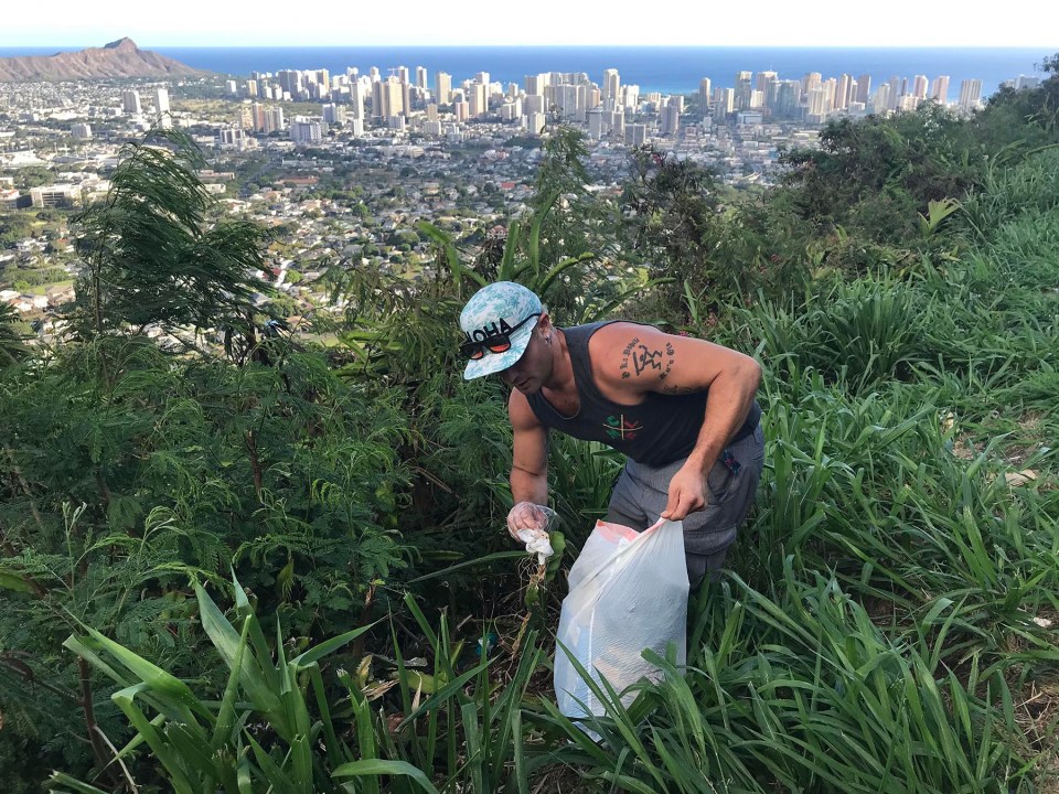 Nick Freitas takes a moment to pick up rubbish from a scenic overlook on Tantalus Drive in Honolulu, while there to watch the sunset, Saturday, August 28, 2021. (Ronen Zilberman photo Civil Beat)