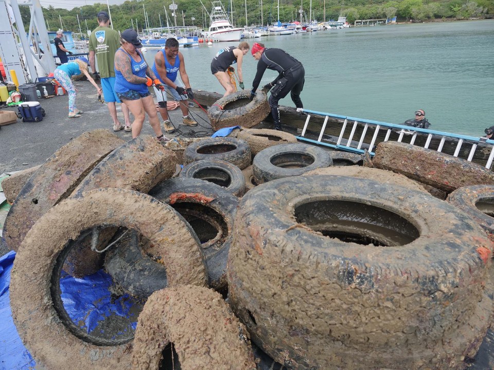 volunteers for the Ocean Defenders Alliance (ODA) pull an old tire out of the water at the Kaneohe Harbor, Sunday, September 12, 2021. The group of ODA volunteers retrieved 43 tires from around the dock of the Harbor Master in Kaneohe Bay. (Ronen Zilberman photo Civil Beat)