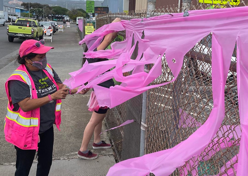 Desiree Somera a volunteer with Statewide Safety Systems hangs pink ribbons in preparation for a drive-thru event to raise awareness and celebrate survivors of breast cancer in Mapunapuna, on Saturday, October 16, 2021. The Statewide Safety Systems Drive-thru: Making Strides Community Adventure event was hosted in partnership with the American Cancer Society.  (Ronen Zilberman photo Civil Beat)