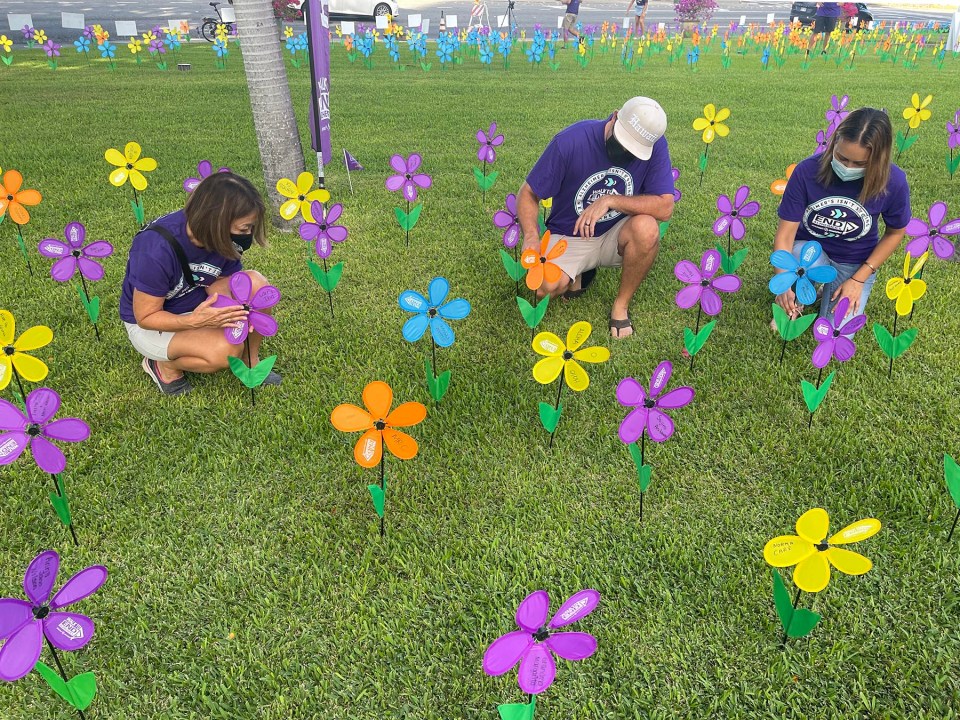 From left: People from the Alzheimer’s Association annual Walk to End Alzheimer’s, Naomi Suto, Douglas Bassett, and Dr. Poki'i Balaz, place flowers that represent those affected by the disease into the Promise Garden on the grassy lawn of Restaurant Row in Honolulu, November 6, 2021.  The yellow flowers honor caregivers, the blue flowers represent those who are currently living with Alzheimer’s and other dementia, the orange flowers celebrate all who support the cause, and the purple flowers represent those that we remember who passed away from the disease. (Ronen Zilberman photo Civil Beat)