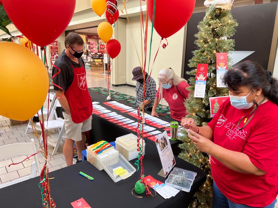Rob Anderson (left) volunteers with the Salvation Army helping Kamlain Louis (right) an employee with the Salvation Army, to set up a table for their Angel Tree Christmas gift donation drive at Kahala Mall, Thursday, December 16, 2021.  People are invited to purchase a requested gift of a child or Kupuna in need and fulfill their Christmas wish for this holiday season. (Ronen Zilberman photo Civil Beat)