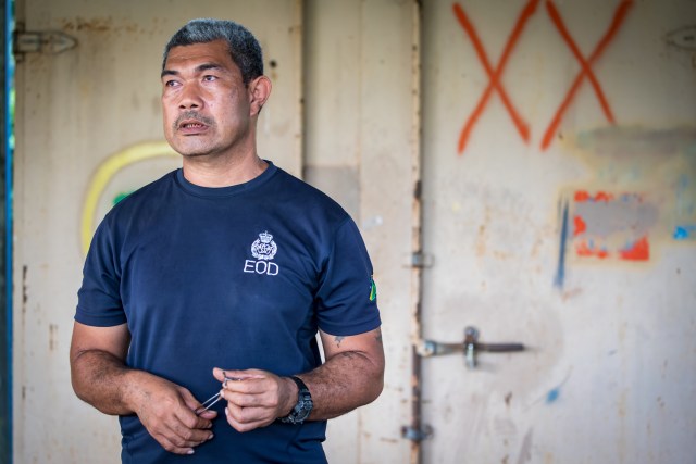 Clifford Tunuki stands in front of a explosive depot. Police Inspector Clifford Tunuki leads a busy team of explosive ordnance technicians, one that he estimates will take decades just to clear the area surrounding his compound. 
