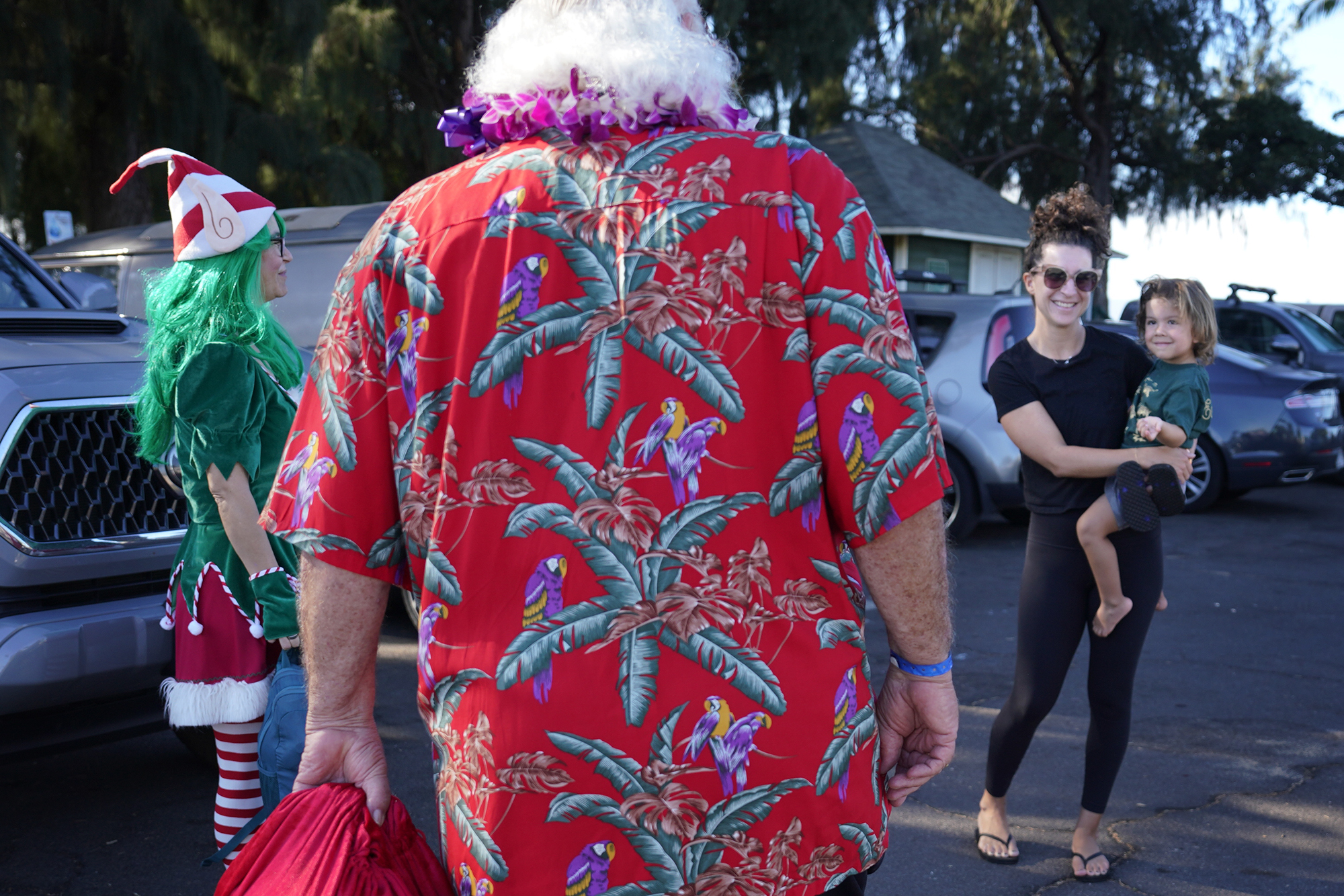 Santa Claus (Ron Proctor) holds the attention of Franklin Yulo, 2 of Kihei, as he returns to his Santa Claus duties on Black Friday, Nov. 24, 2023, in Kihei. Proctor has played Santa for more than 25 years. He lost his Lahaina home and belongings, including the hand-made Santa suit his daughter made, in the Aug. 8 fire. Jackie Yulo holds Franklin. (Kevin Fujii/Civil Beat/2023)