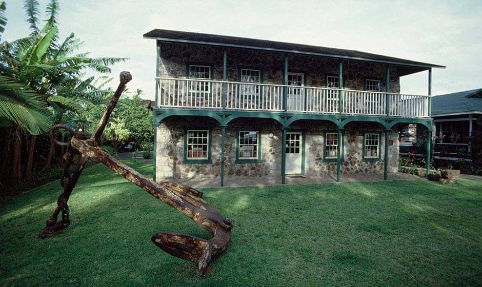 The 2-story Seamans Hospital building on a grassy lawn behind a large rusty anchor.