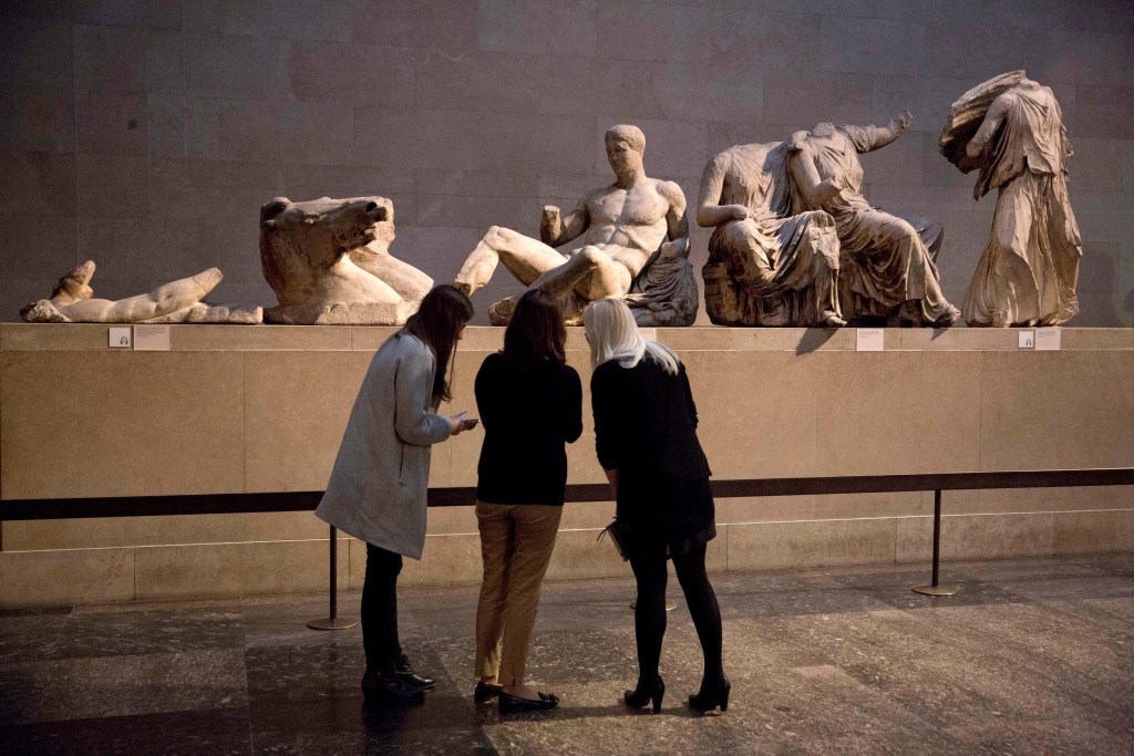 FILE - Women stand by a marble statue of a naked youth thought to represent Greek god Dionysos, center, from the east pediment of the Parthenon, on display during a media photo opportunity to promote a forthcoming exhibition on the human body in ancient Greek art at the British Museum in London, on Jan. 8, 2015. The chairman of the British Museum said Thursday, Feb. 16, 2023 the U.K. and Greece are working on a deal that would see the Parthenon Marbles displayed in both London and Athens. The antiquities, also known as the Elgin Marbles, are the remnants of a frieze that ran around the outer walls of the Parthenon temple on the Acropolis in Athens. (AP Photo/Matt Dunham, File)