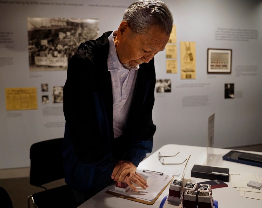 Kazuo Fujii puts his weight into a commemorative stamp after placing a Japanese hanko (stamp) on his and his relatives names in the Ireichō Thursday, April 9, 2026, in Honolulu. (Kevin Fujii/Civil Beat/2026)