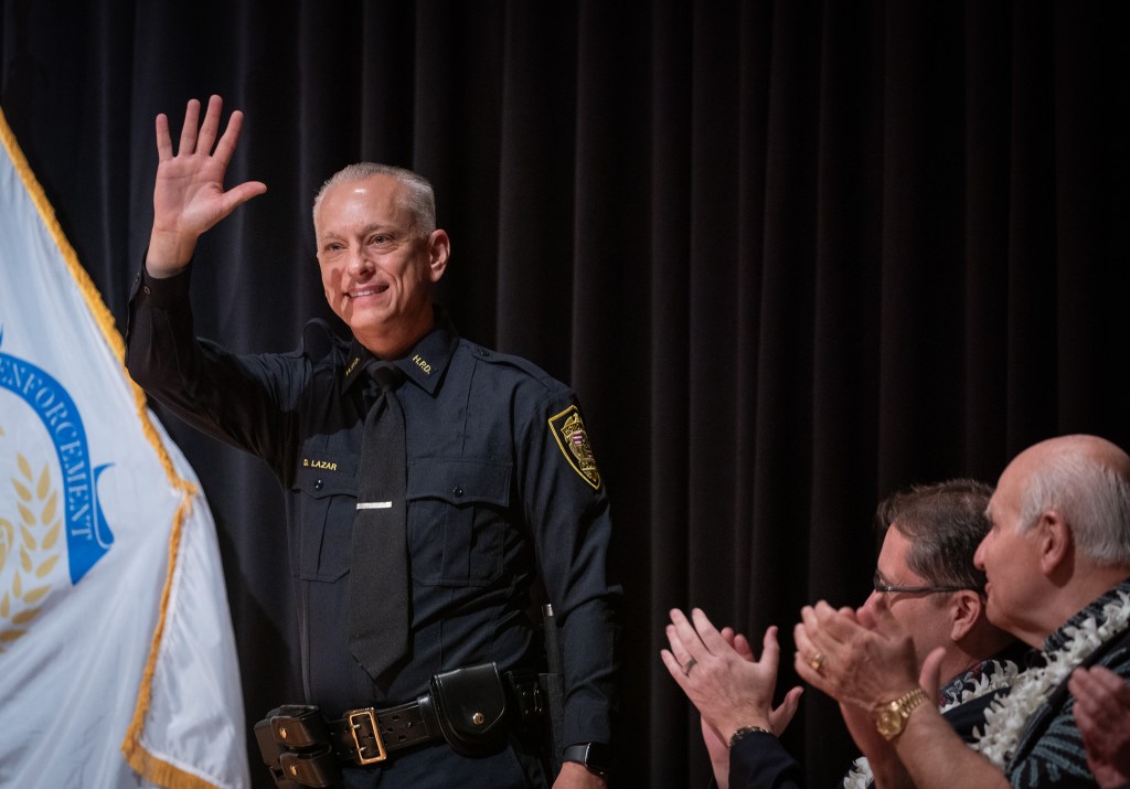 New HPD Chief David Lazar waves to the audience at his swearing in ceremony at Memorial Auditorium in Honolulu July 2, 2026. Seated at right is Mayor Rick Blangiardi and acting Lt. Gov. Keith Regan. (Craig Fujii/Civil Beat/2026)